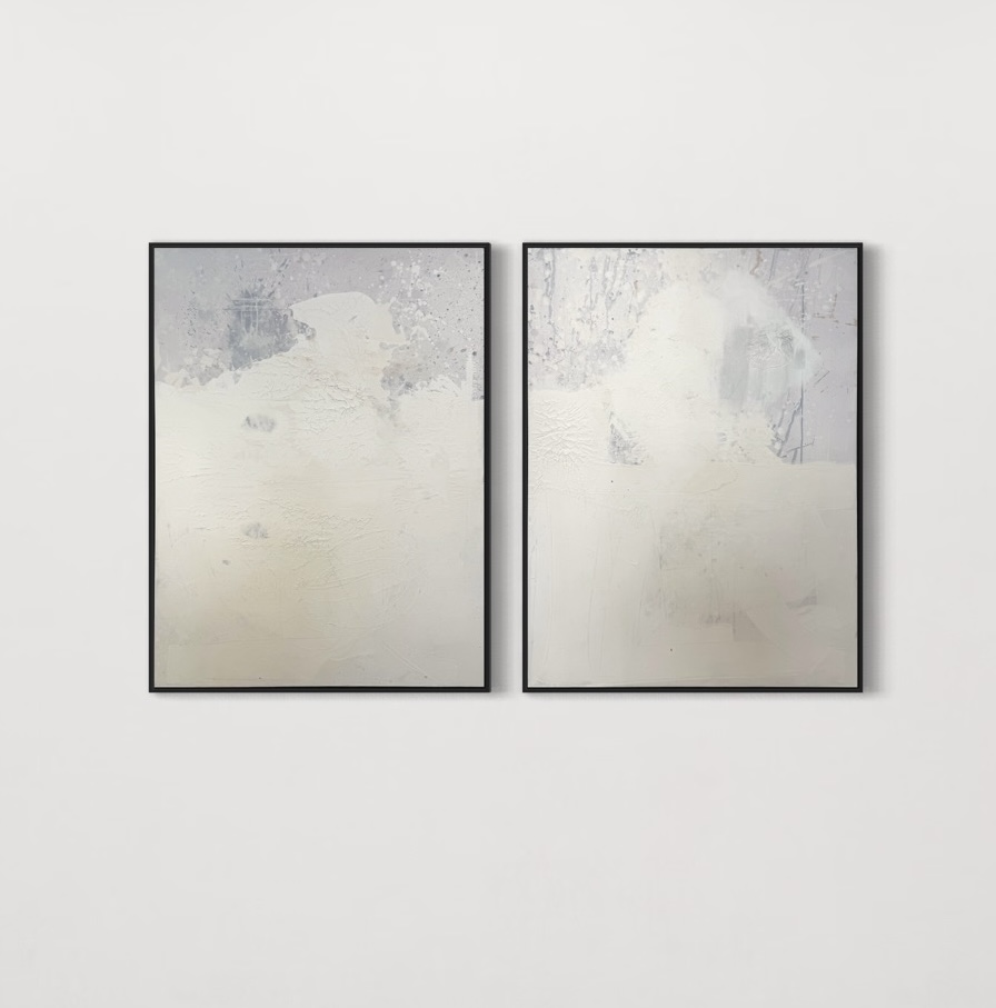 A two-panel abstract diptych titled "Soft Awakening" by Gina Keatley, featuring muted whites, soft grays, and delicate textures that create a serene, atmospheric composition. The surface includes subtle crackling, organic textures, and faint, speckled drips resembling gentle rainfall. The panels are connected through flowing textures and tonal gradations, evoking a sense of calm transition and renewal. Thin black frames encase each panel, enhancing the minimalist aesthetic.