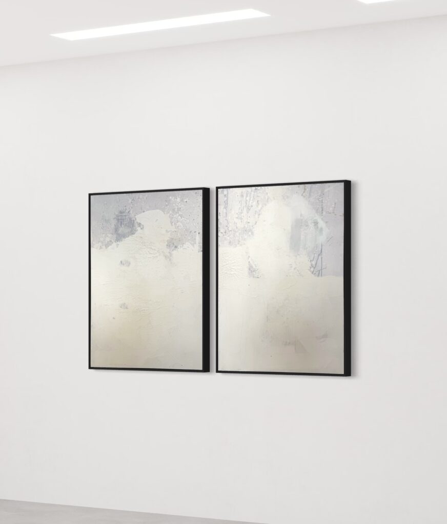 A two-panel abstract diptych titled "Soft Awakening" by Gina Keatley, featuring muted whites, soft grays, and delicate textures that create a serene, atmospheric composition. The surface includes subtle crackling, organic textures, and faint, speckled drips resembling gentle rainfall. The panels are connected through flowing textures and tonal gradations, evoking a sense of calm transition and renewal. Thin black frames encase each panel, enhancing the minimalist aesthetic.